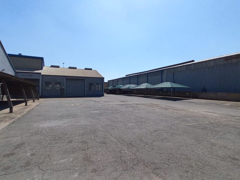 Spacious industrial yard featuring asphalt surfacing, corrugated metal warehouse structures, a covered loading area, and perimeter boundary walls.