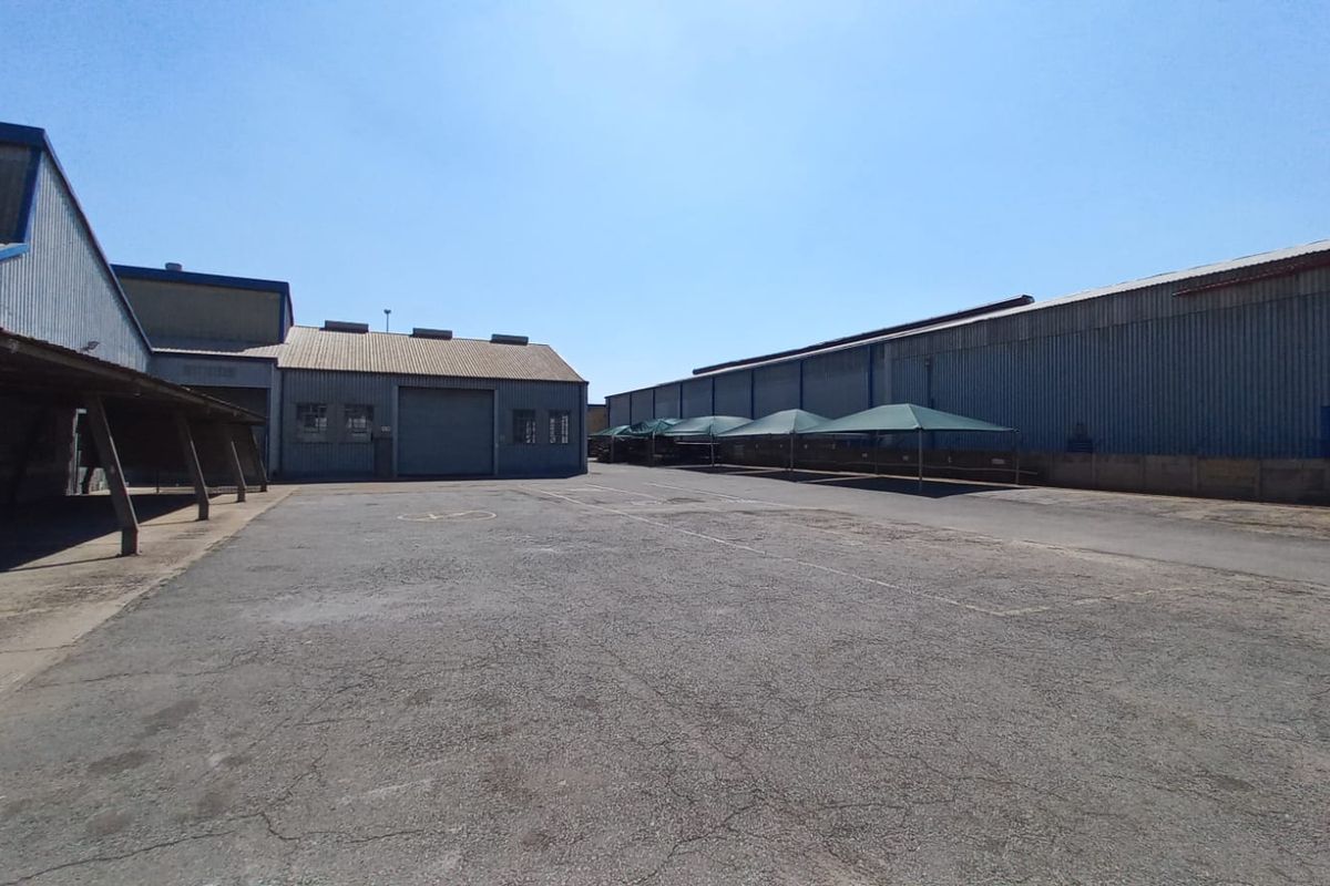 Spacious industrial yard featuring asphalt surfacing, corrugated metal warehouse structures, a covered loading area, and perimeter boundary walls.