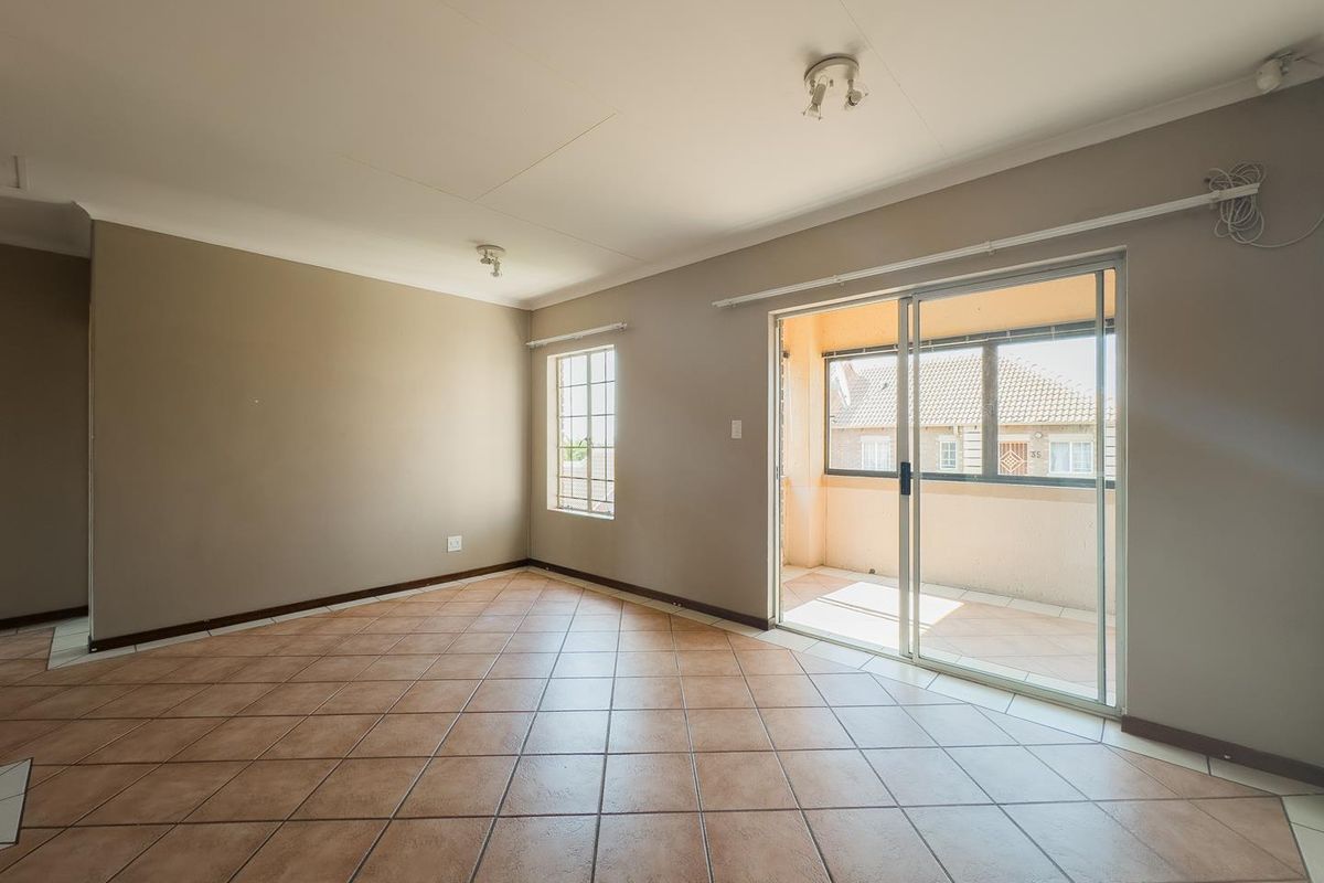 Spacious living area featuring neutral wall tones, ceramic floor tiles, and large sliding glass doors providing direct access to a private balcony.
