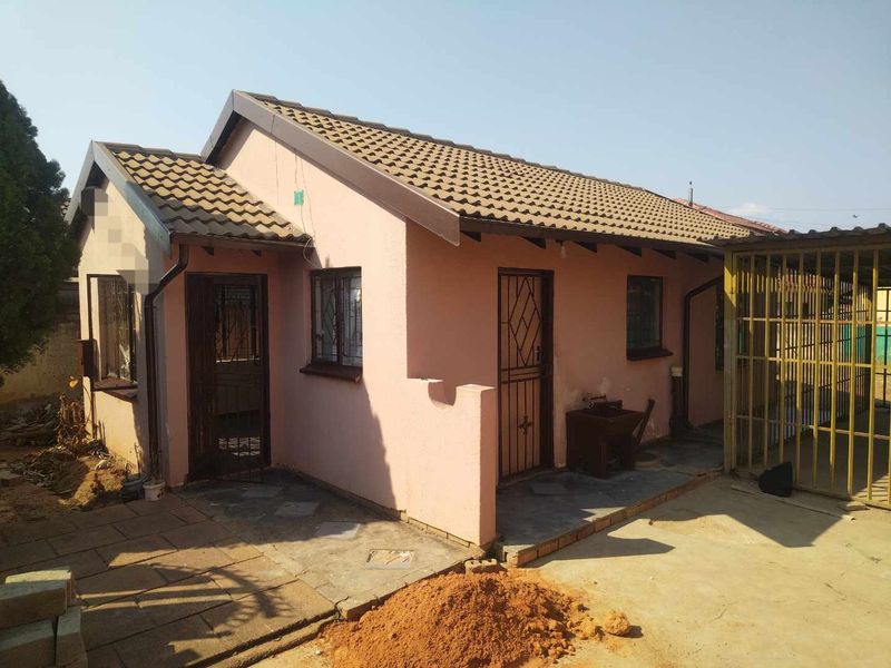 Front exterior view of a single-story house featuring a tiled roof, security gates, and an attached carport with paved driveway area.