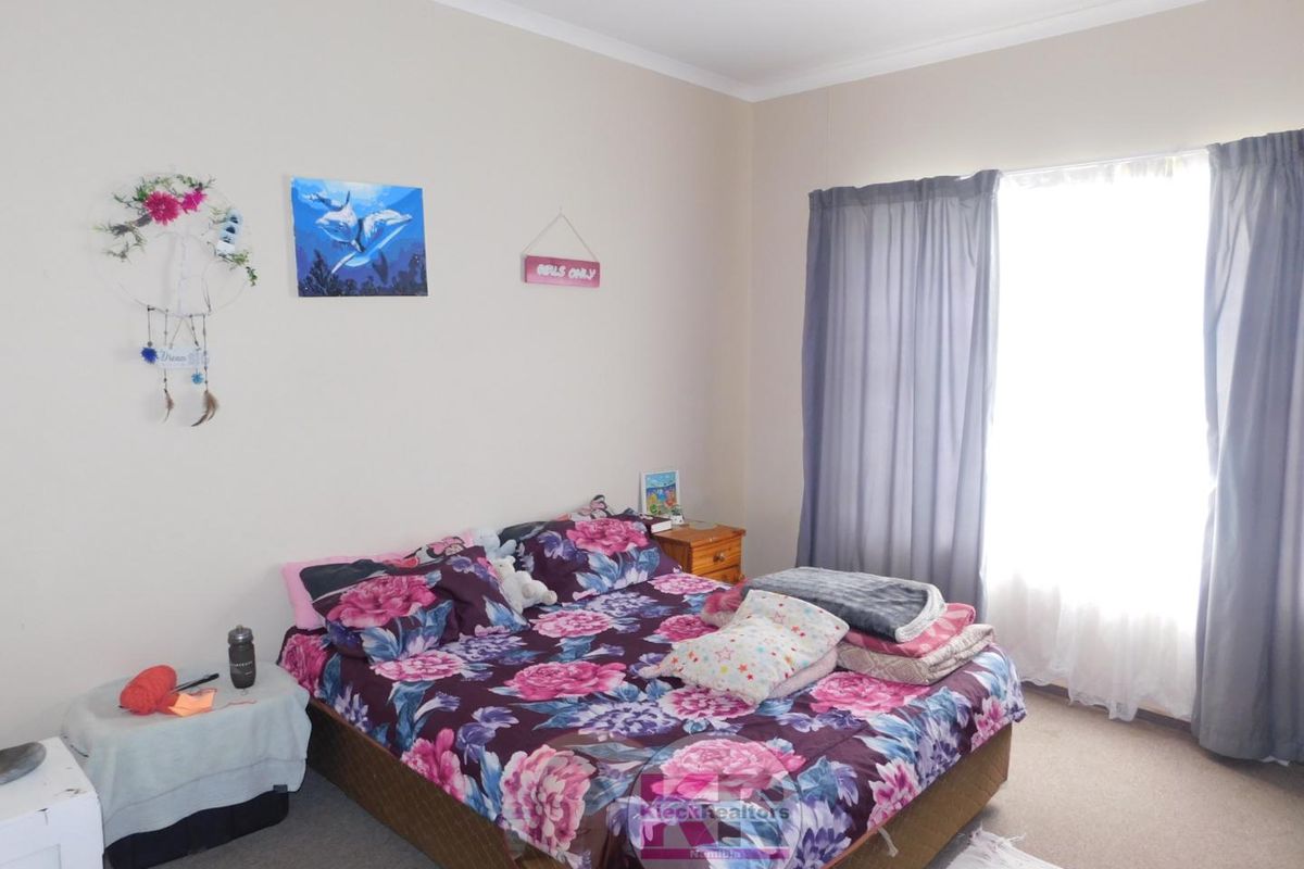A standard bedroom featuring neutral wall finishes, carpeted flooring, and a large window with curtain treatments.