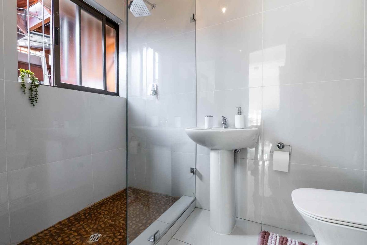 Modern bathroom featuring a pedestal sink, a glass-enclosed shower with a pebble floor, and white wall tiling.