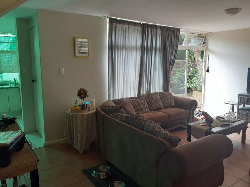 A living room area featuring tiled flooring and a large sliding glass door providing access to the garden, with an adjacent view into the kitchen.