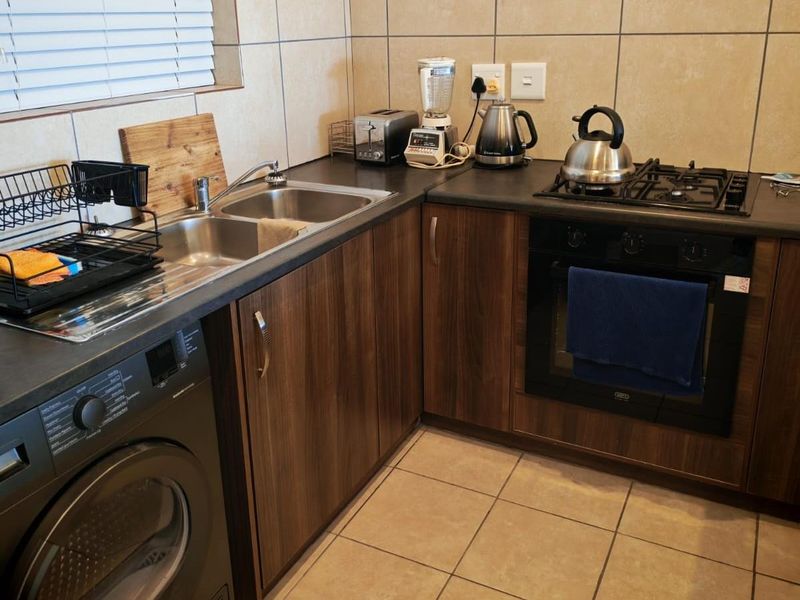 A functional kitchen featuring dark wood-look cabinetry, dark countertops, a built-in oven with gas hob, and a double sink with tiled backsplash.