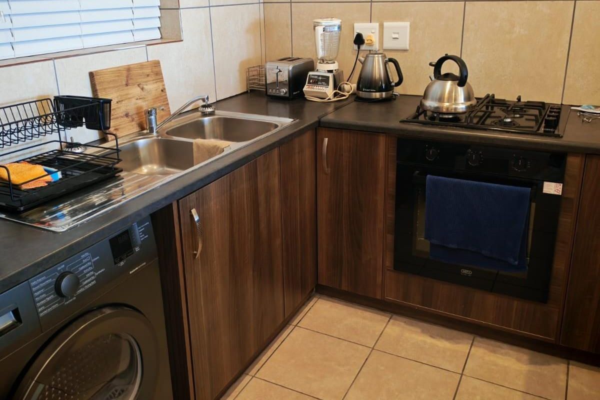 A functional kitchen featuring dark wood-look cabinetry, dark countertops, a built-in oven with gas hob, and a double sink with tiled backsplash.