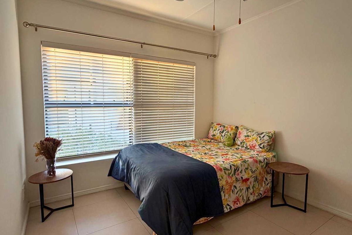 A functional bedroom featuring tiled flooring, a ceiling fan, and large windows fitted with venetian blinds for natural light control.