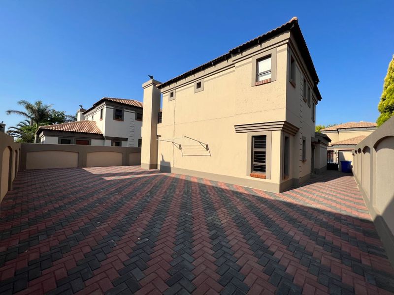 A well-maintained rear exterior area featuring a paved courtyard, boundary walls, and a multi-story building facade with a tiled roof.