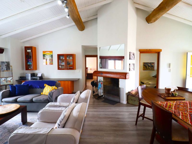 Spacious open-plan living and dining area featuring vaulted ceilings with exposed timber beams, laminate flooring, and a central built-in fireplace with a timber mantel.