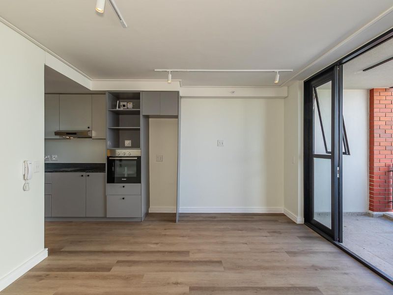 Modern open-plan living area featuring sleek grey cabinetry, integrated oven, laminate flooring, and large sliding doors leading to a private balcony.