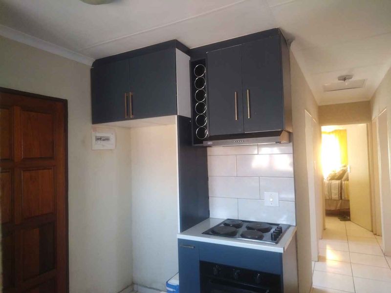 A compact kitchen area featuring dark blue built-in cabinetry, a built-in oven with hob, extractor fan, and tiled backsplash.