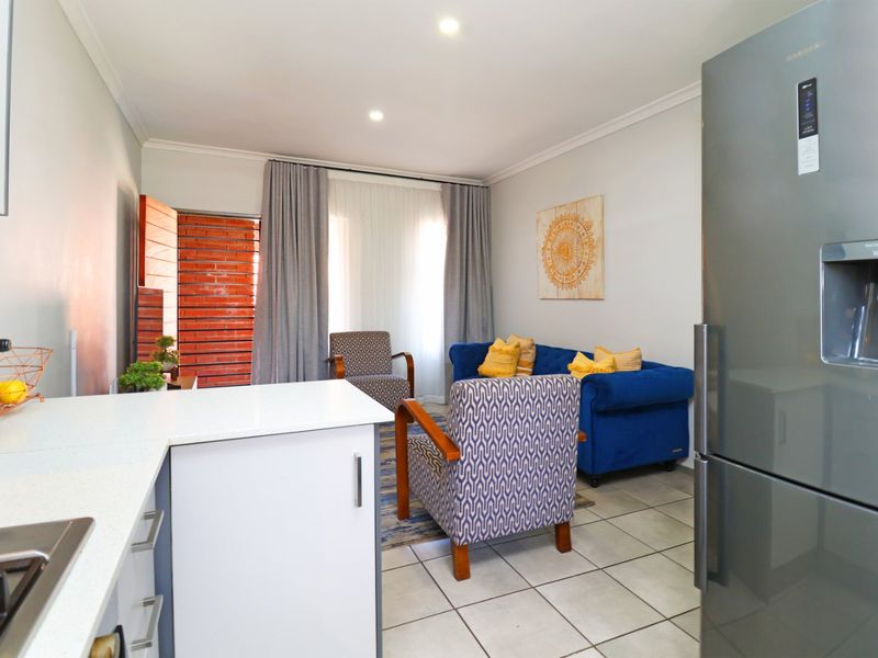 Open-plan living area featuring a modern kitchen with stone countertops, gas hob, and tiled flooring, seamlessly flowing into a comfortable lounge space.