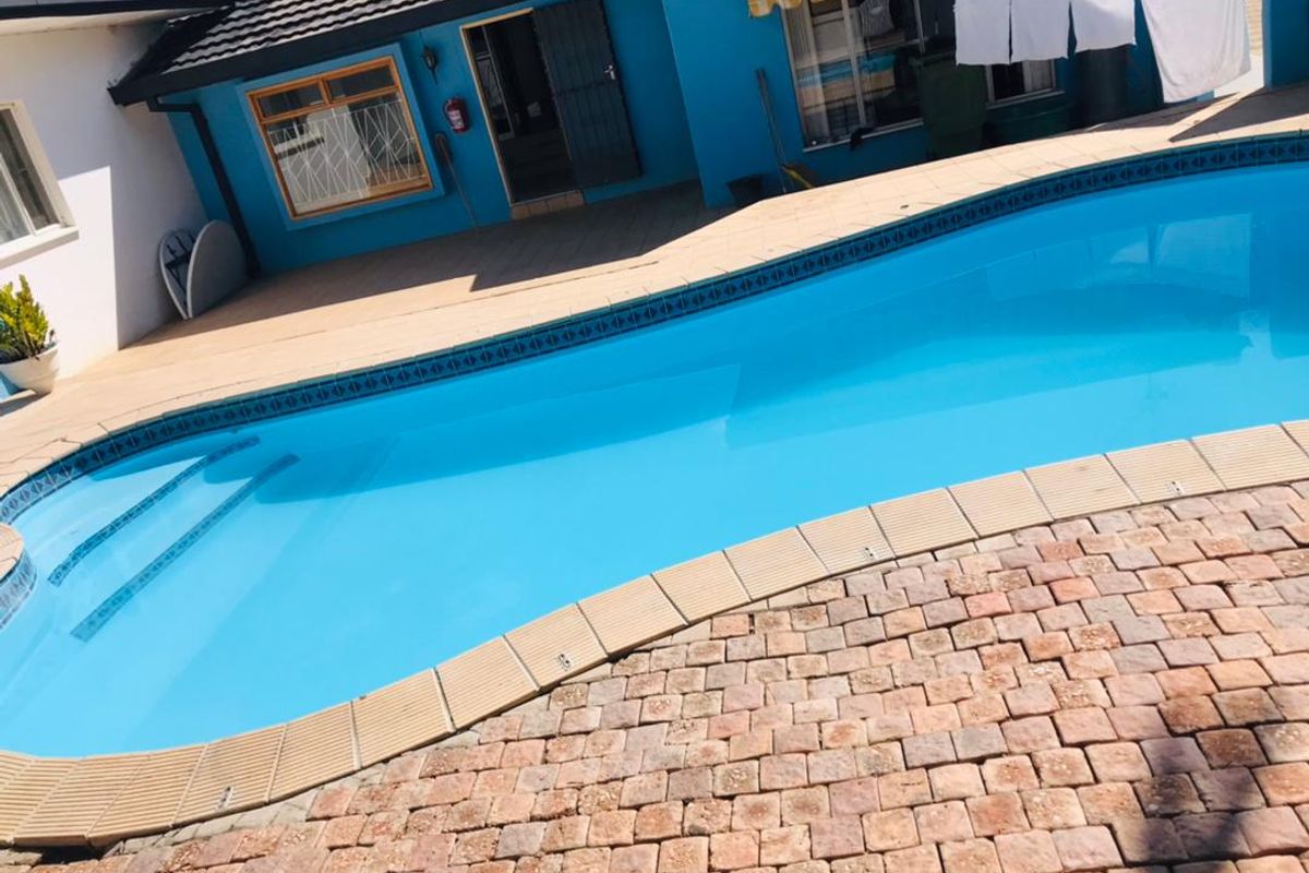 Outdoor pool area featuring a swimming pool with tiled coping and paved patio space, adjacent to the main building structure.