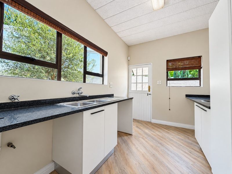 A clean and functional scullery featuring granite countertops, double stainless steel sink, laminate flooring, and a stable door leading to the exterior.
