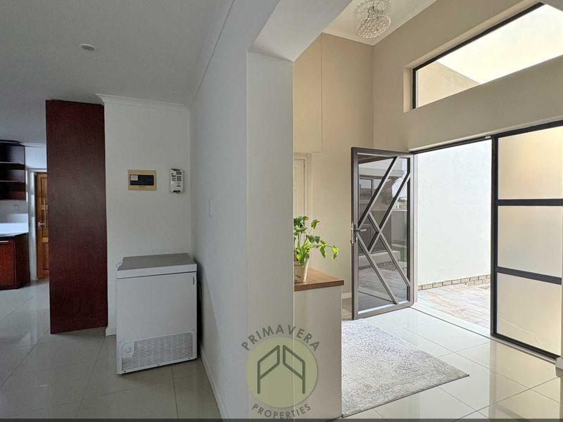 Bright entrance hall featuring high ceilings with clerestory windows, tiled flooring, and an open-plan layout leading into the kitchen area.