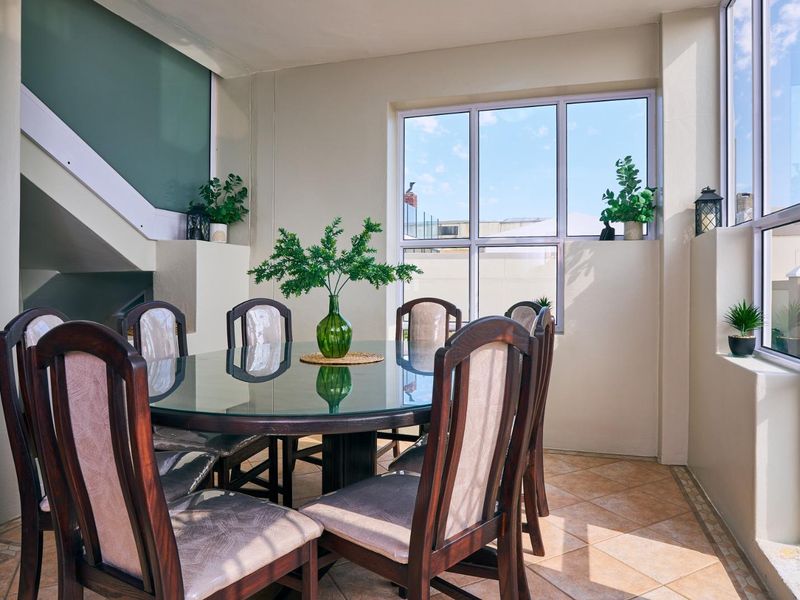 A bright dining area featuring large windows, tiled flooring, and an open staircase, providing a functional space for family meals.