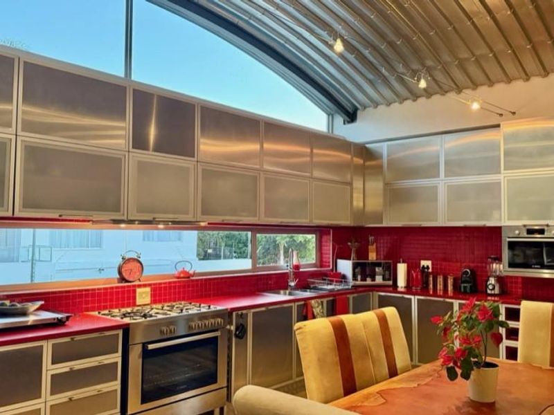 Modern kitchen featuring stainless steel cabinetry, vibrant red tiled backsplash, gas cooktop, built-in oven, and a unique curved metal ceiling with track lighting.
