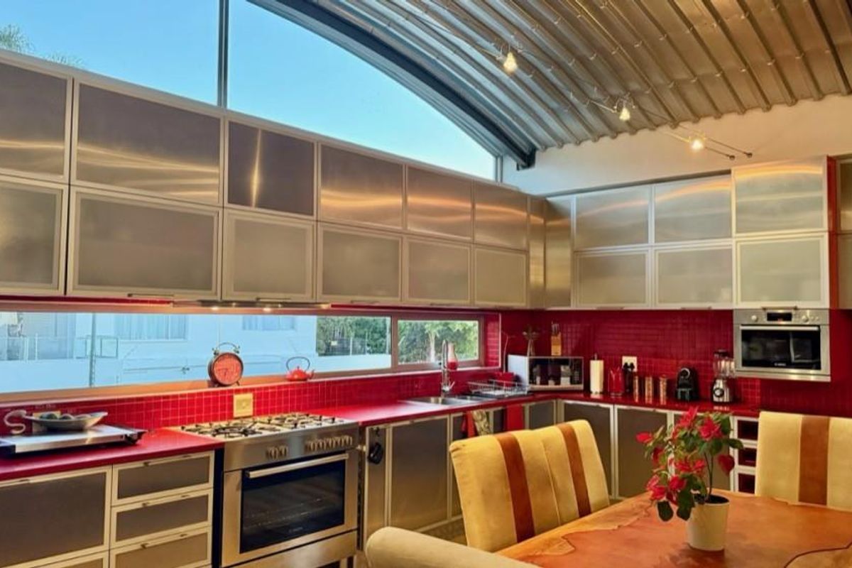 Modern kitchen featuring stainless steel cabinetry, vibrant red tiled backsplash, gas cooktop, built-in oven, and a unique curved metal ceiling with track lighting.