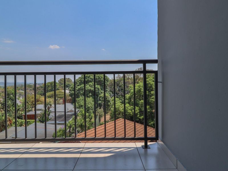 A clean, open balcony featuring tiled flooring and a secure metal balustrade, offering an elevated view of the surrounding neighborhood and greenery.
