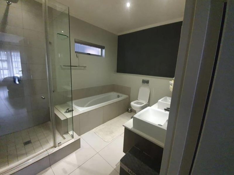 Modern bathroom featuring a glass-enclosed shower, built-in bathtub, wall-mounted toilet, and a double vanity with contemporary fixtures.