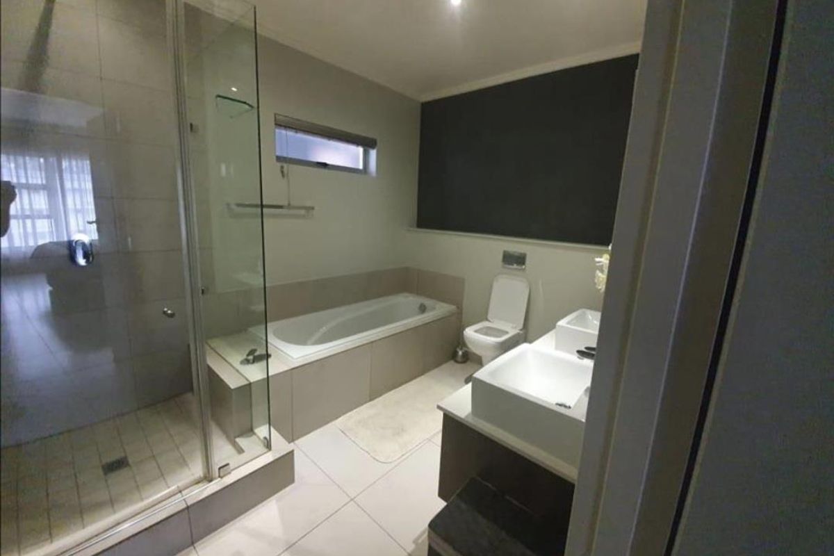 Modern bathroom featuring a glass-enclosed shower, built-in bathtub, wall-mounted toilet, and a double vanity with contemporary fixtures.