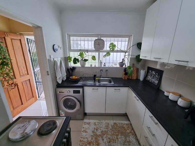 Compact kitchen featuring white cabinetry, dark countertops, a built-in washing machine, and an electric stove with a tiled backsplash.