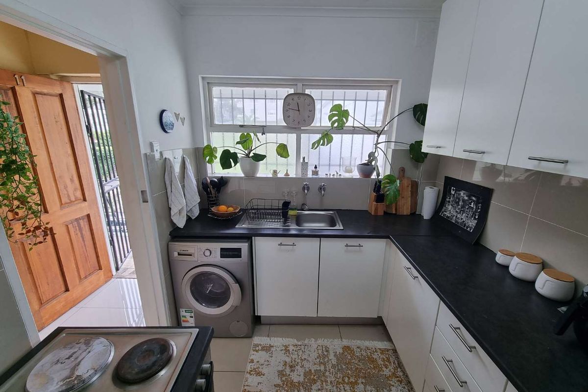 Compact kitchen featuring white cabinetry, dark countertops, a built-in washing machine, and an electric stove with a tiled backsplash.