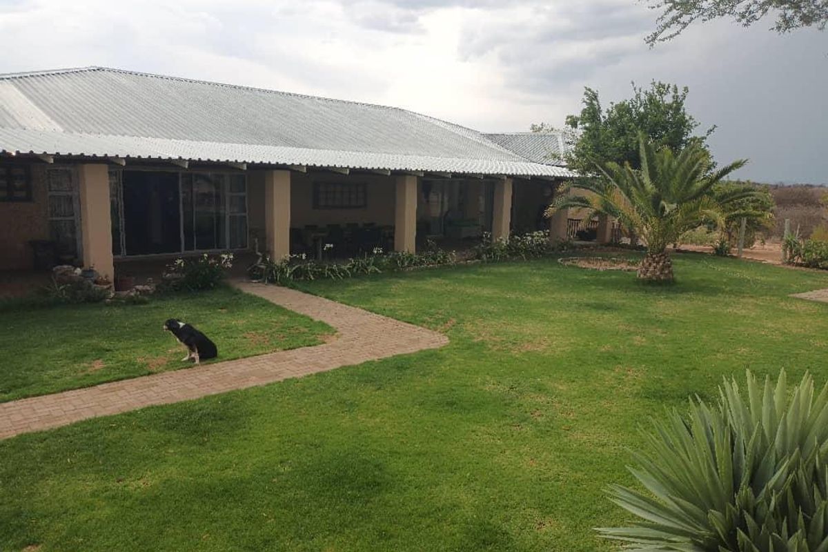 A spacious rear exterior view featuring a covered patio, a well-maintained lawn, and a paved walkway leading to the house.