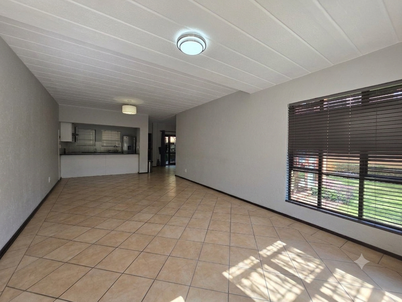 Spacious open-plan living and kitchen area featuring neutral tiled flooring, built-in cabinetry, and large windows with venetian blinds.