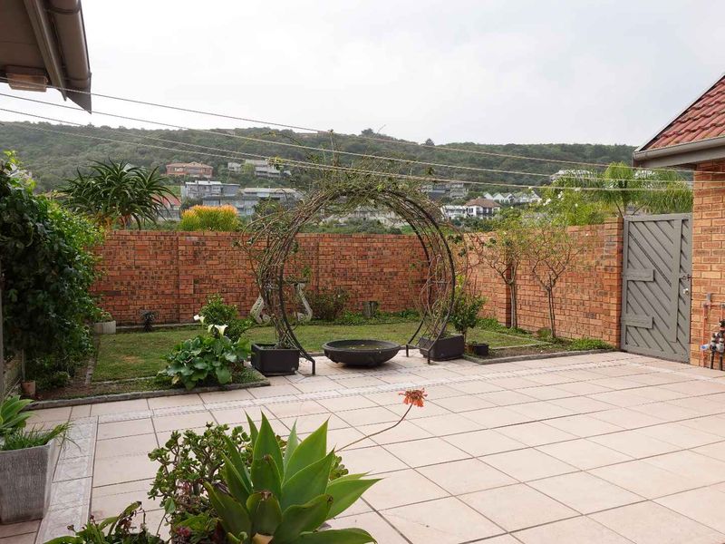 A private rear garden featuring a paved patio area, brick boundary walls, and a landscaped lawn with established garden features.