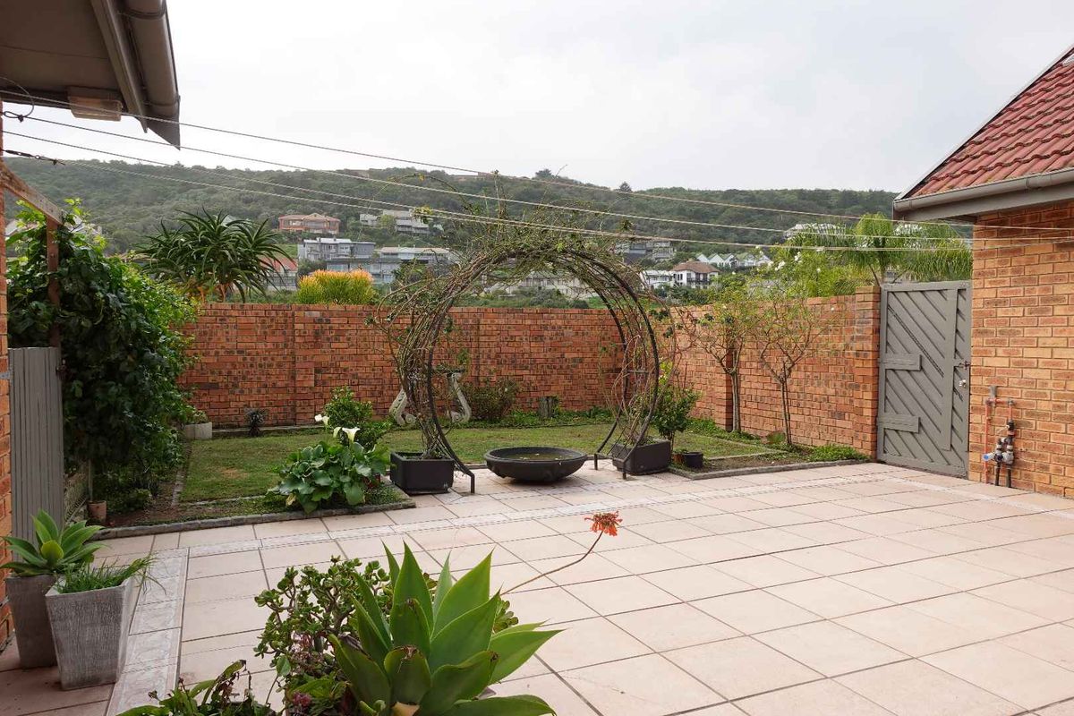 A private rear garden featuring a paved patio area, brick boundary walls, and a landscaped lawn with established garden features.