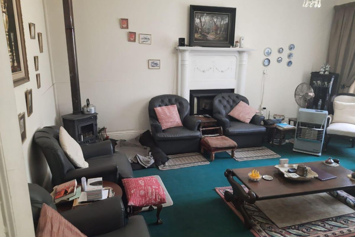 A traditional living room featuring a classic fireplace mantel and a freestanding wood-burning stove, providing a cozy and functional living space.
