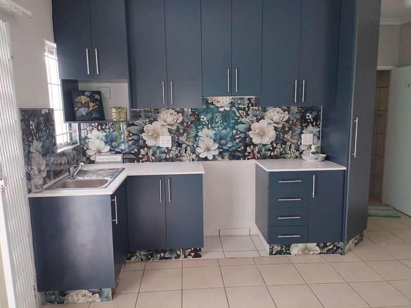 A modern kitchen featuring dark blue cabinetry, white countertops, and a distinctive floral splashback, complemented by neutral floor tiles.