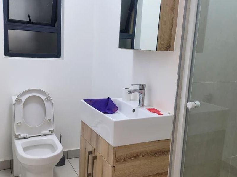 A modern bathroom featuring a vanity cabinet with a ceramic basin, a toilet, and a glass-enclosed shower with tiled flooring.