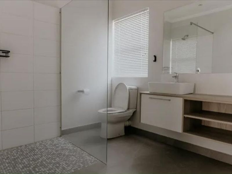 Modern bathroom featuring a walk-in shower with glass screen, wall-mounted vanity with vessel sink, and neutral tiling throughout.