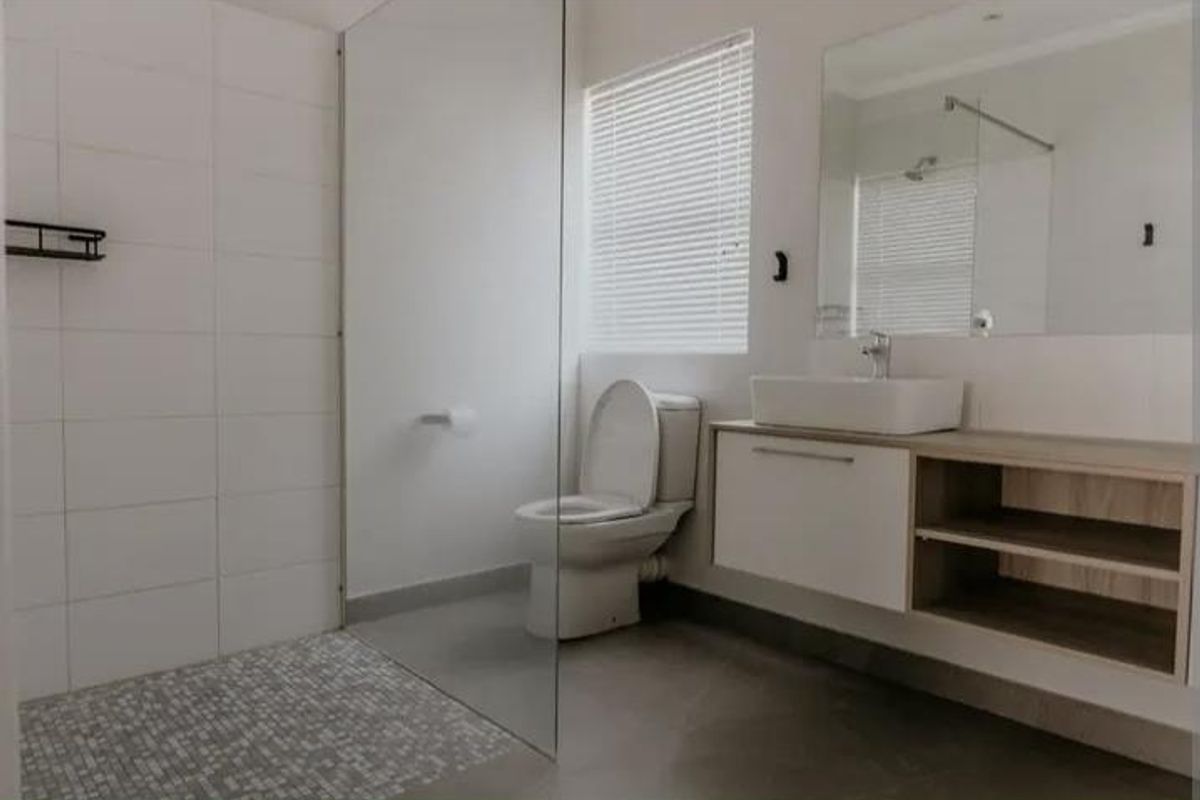 Modern bathroom featuring a walk-in shower with glass screen, wall-mounted vanity with vessel sink, and neutral tiling throughout.