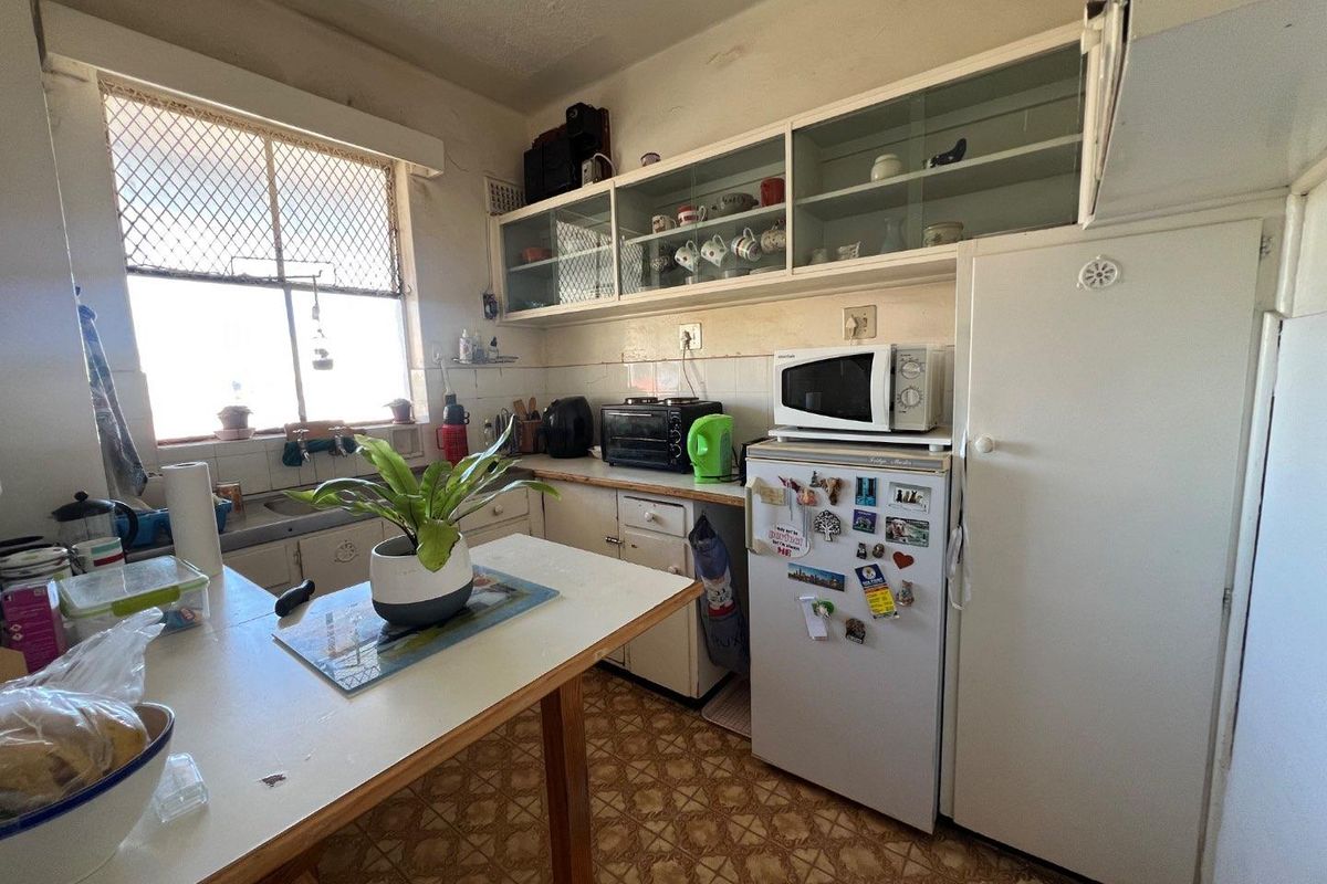 A dated kitchen featuring original cabinetry, glass-fronted upper storage, and a tiled backsplash, offering significant potential for modernization and renovation.