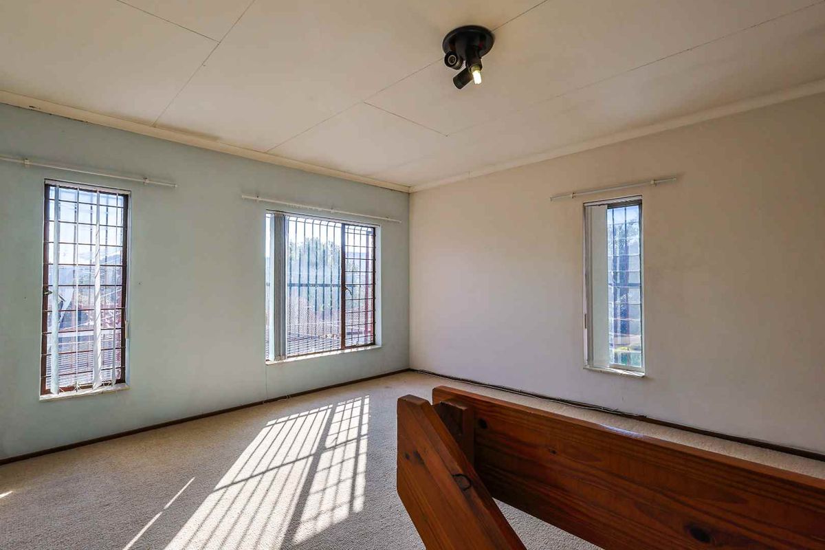 An empty bedroom featuring carpeted flooring, multiple windows with security bars, and a wooden staircase railing.