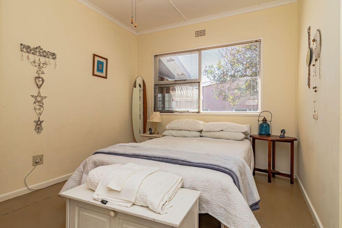 A functional bedroom featuring a window with venetian blinds and neutral wall finishes, offering a comfortable space for rest.