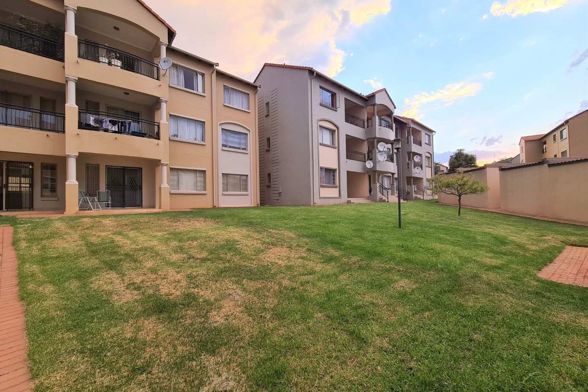 View of the apartment complex rear elevation featuring communal lawn areas, paved walkways, and private balconies with satellite dish installations.