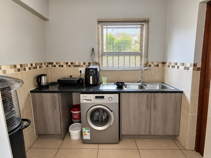 A functional laundry area featuring built-in cabinetry, granite countertops, a stainless steel double sink, and tiled finishes.