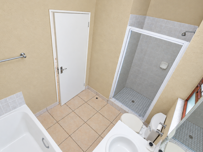 A functional bathroom featuring a built-in bathtub, separate shower enclosure, vanity sink, and toilet with neutral tiled flooring and wall finishes.