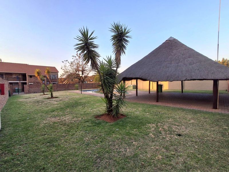Communal outdoor area featuring a swimming pool, a large thatched lapa for shade, and paved surrounds within a secure complex.