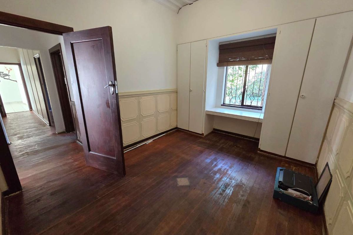 A vacant bedroom featuring original timber flooring, built-in cupboards, wainscoting, and an ornate ceiling, offering a classic foundation for renovation.