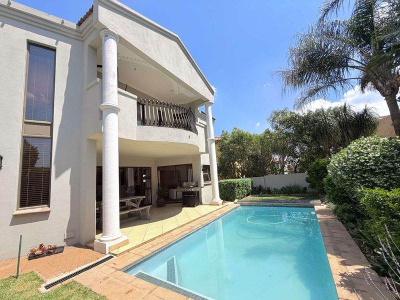 Rear exterior view featuring a swimming pool, covered patio area with columns, and an upper-level balcony overlooking the garden.