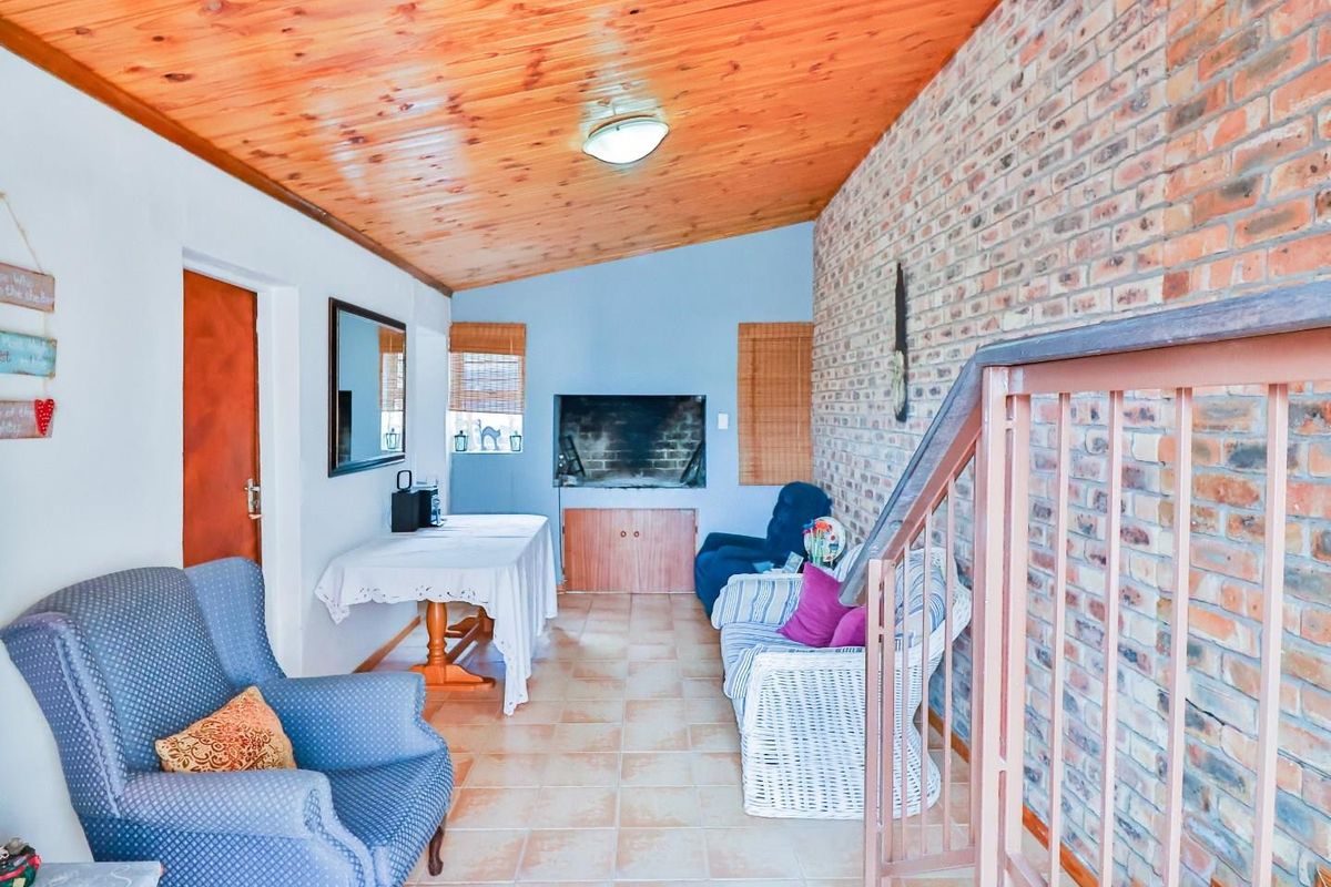 A living area featuring a rustic exposed brick wall, tiled flooring, and a timber-clad raked ceiling with an integrated staircase.