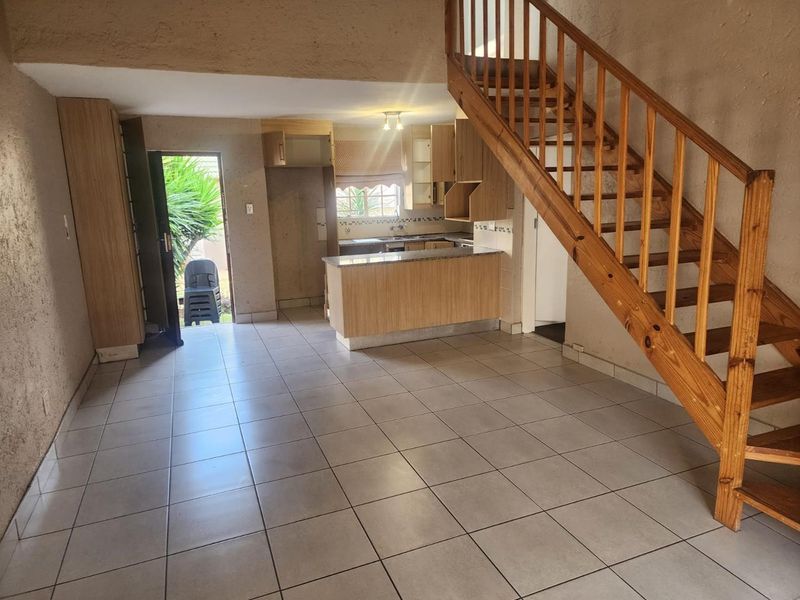 Open plan living area featuring tiled floors, a wooden staircase, and a functional kitchen with built-in cabinetry and a peninsula.