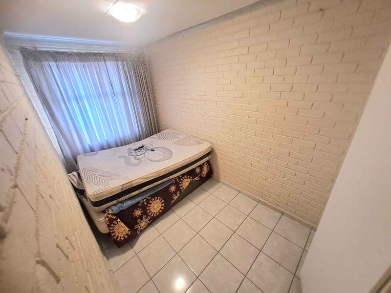 A compact bedroom featuring tiled flooring and painted brick walls, providing a functional space that could benefit from cosmetic updates.