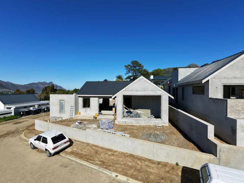 An aerial view of a residential property currently under construction, featuring a metal roof and concrete exterior walls in a developing estate.