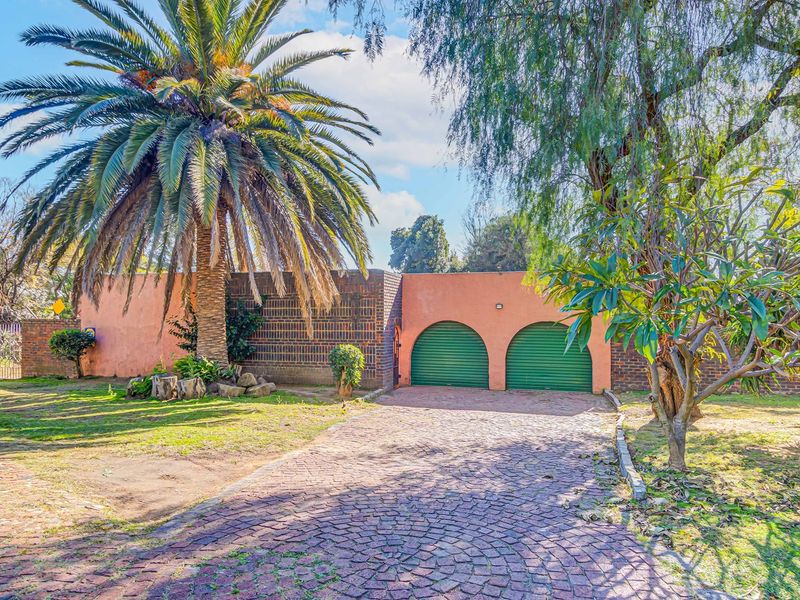 Front view of the property featuring a double garage with roller shutter doors, a cobblestone driveway, and established garden landscaping.