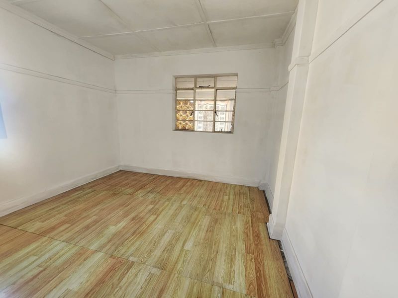 A vacant bedroom featuring timber-look laminate flooring, a central casement window, and a panelled ceiling, offering a blank canvas for renovation.